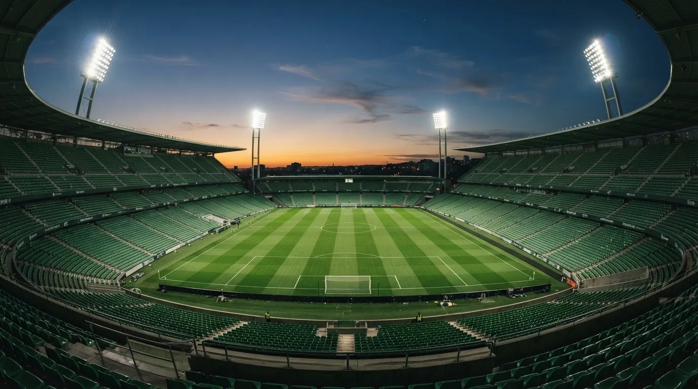 An empty football stadium with floodlight masts at dusk