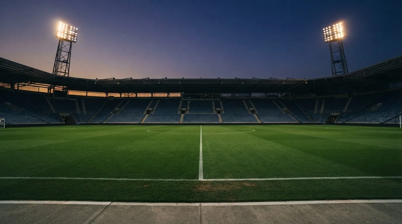 An empty football stadium with floodlight masts at dusk