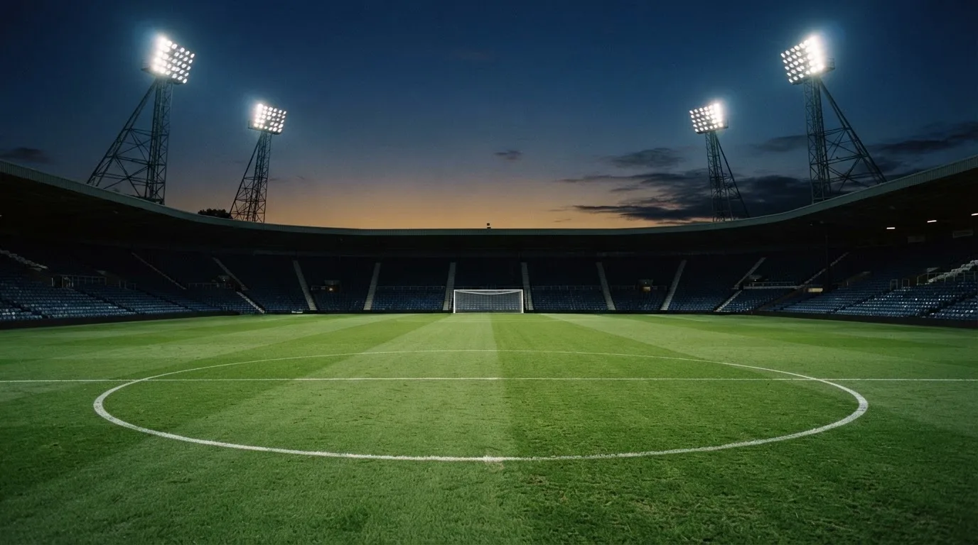 An empty football stadium with floodlight masts at dusk
