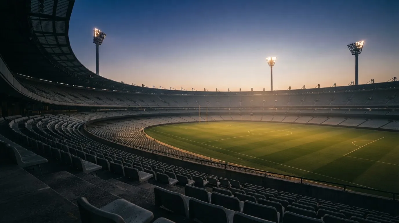 An empty football stadium with floodlight masts at dusk