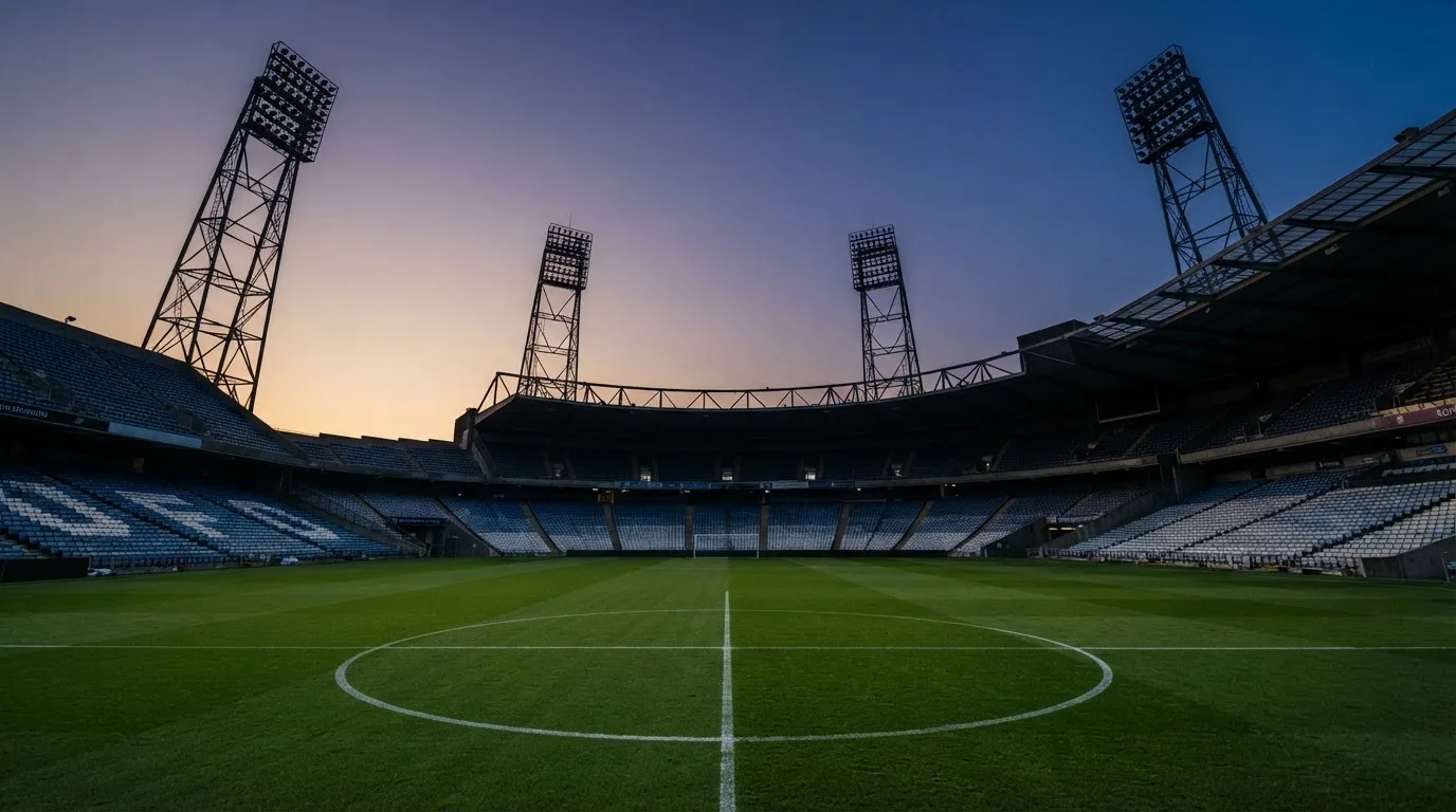 An empty football stadium with floodlight masts at dusk