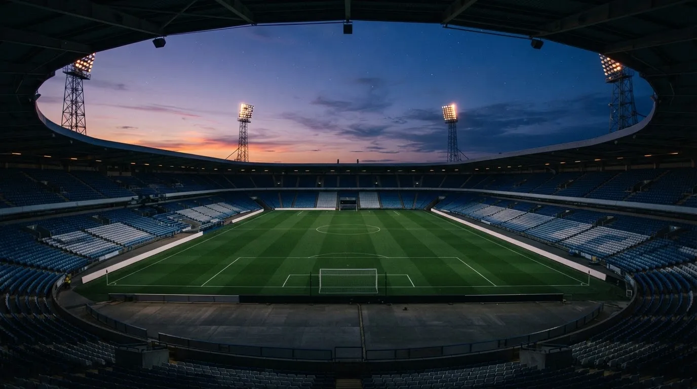 An empty football stadium with floodlight masts at dusk